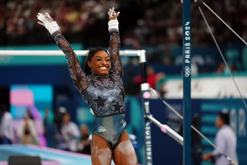 Simone Biles flings her arms up in happiness at the end of a routine in sparkling grey and silver leotard