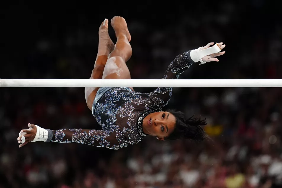 Simone Biles twists in the air as she catches a gymnastics bar 