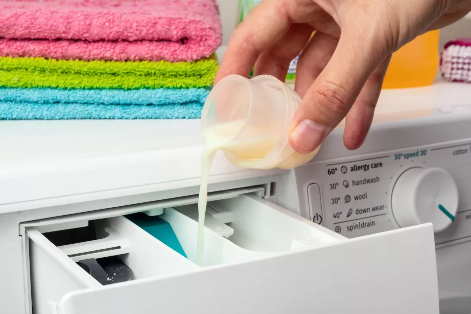 Pouring the laundry conditioner into the washing machine. Laundry concept.