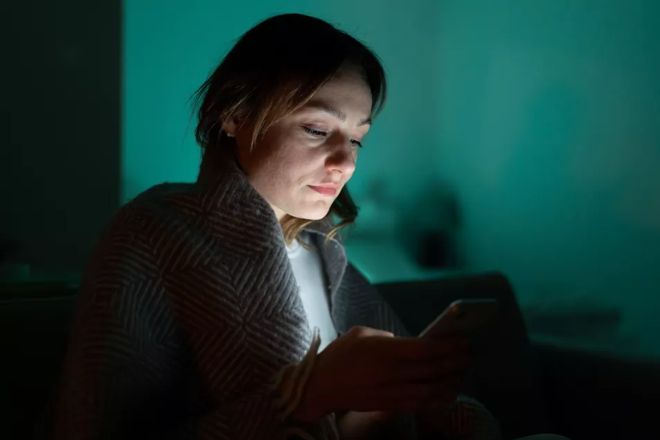 A female scrolling through social networks on mobile phone late at night in dark bedroom.