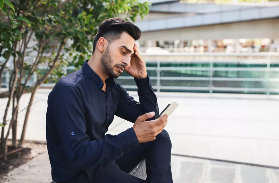 Stressed Middle Eastern business guy using app on phone outside
