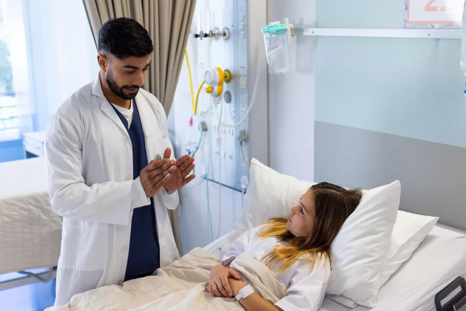 Male doctor with asthma inhaler explaining to girl patient in hospital bed