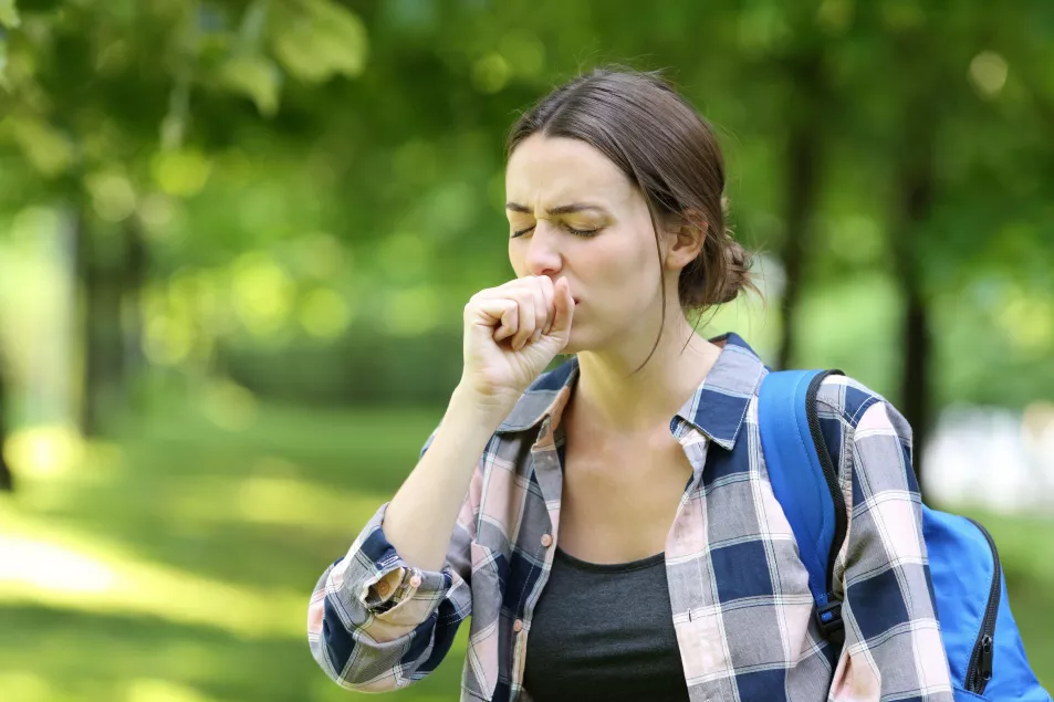 A woman coughing outdoors