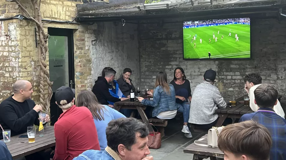 People sitting on wooden tables and benches outside The Mitre pub in London 