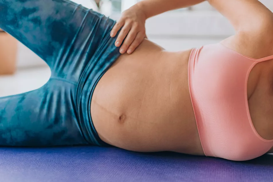 Pregancy pilates side lying clam exercise for pelvic stability and hip muscles training. Pregnant woman working out on floor closeup of expecting