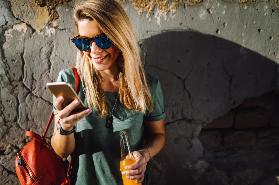 Woman with long blonde hair standing in a sunny street, looking at her phone