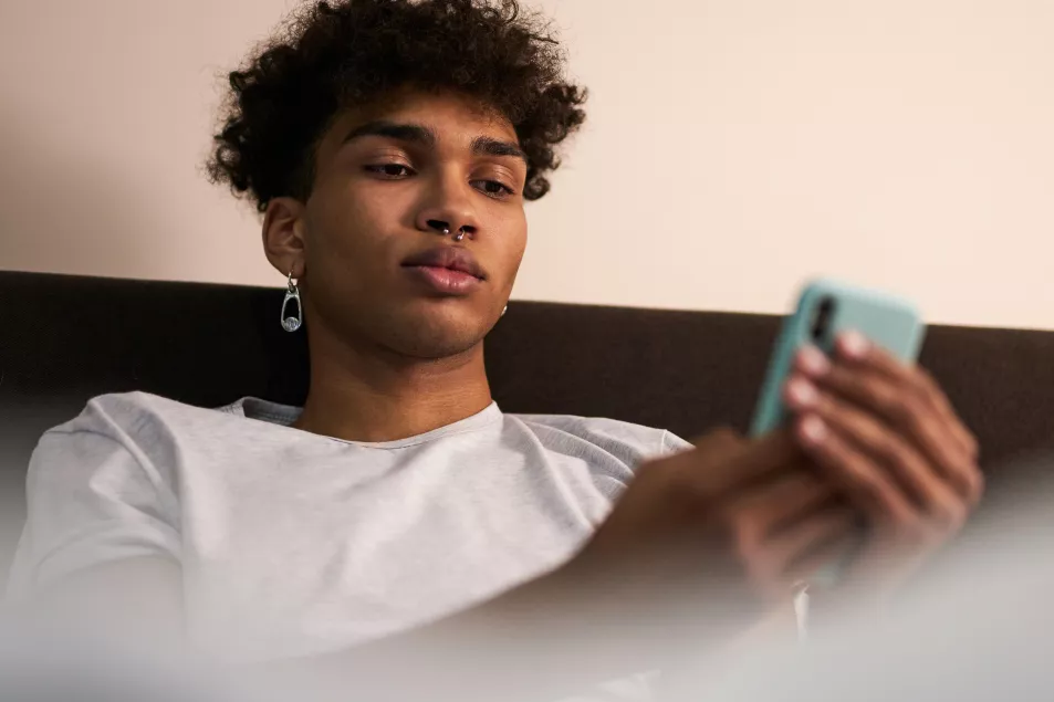 Young black man sitting up in bed looking at his phone