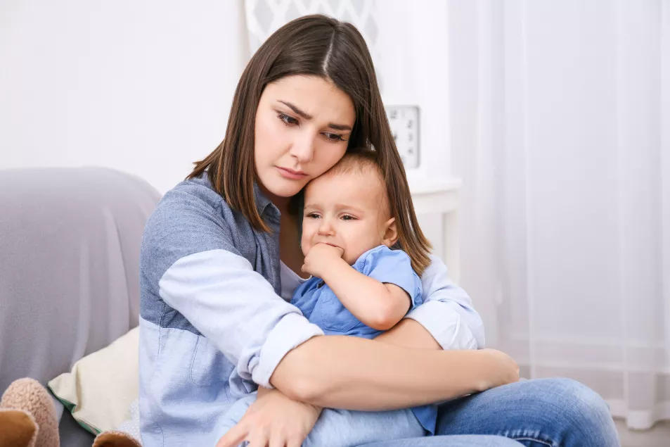 Depressed young woman with cuddling baby at home