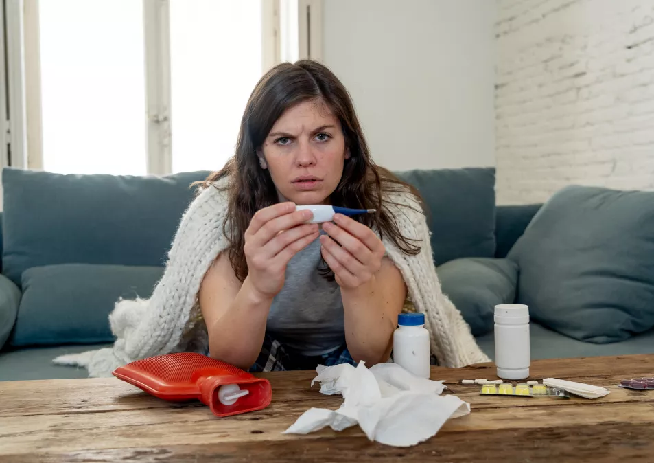 Ill women sat on the sofa with tissue and pain killers suffering from a fever