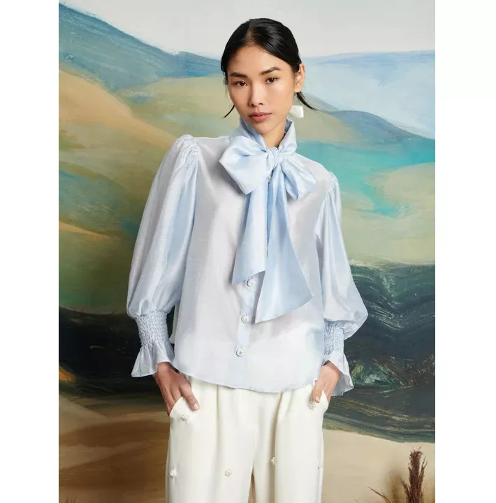 Model wears pale blue pussybow blouse with pearl buttons 