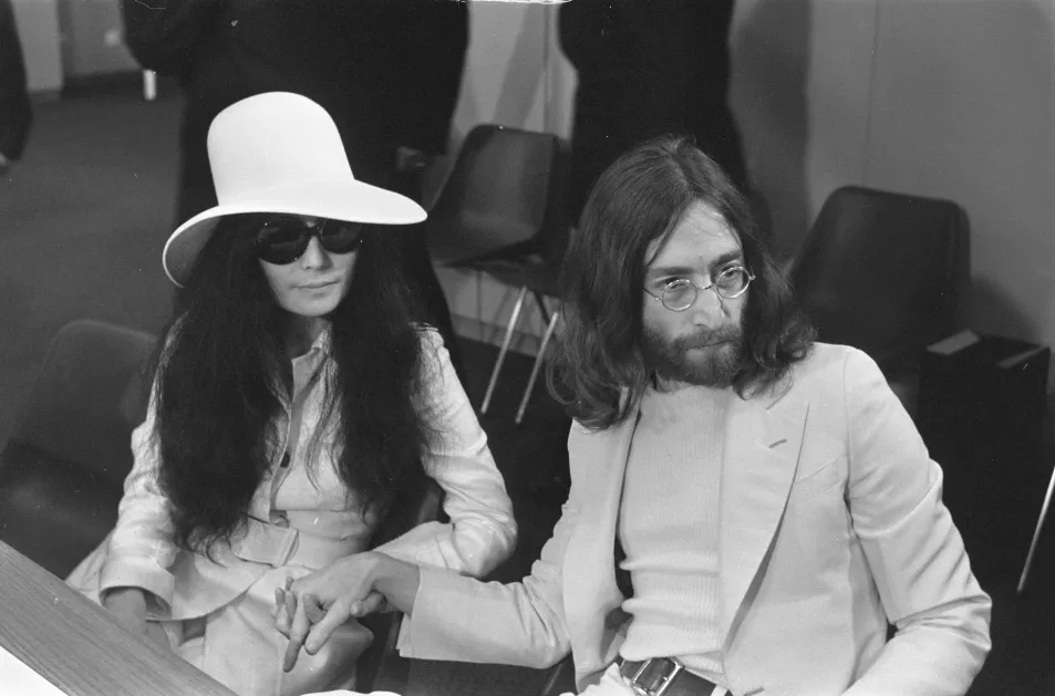 John Lennon and his wife, Yoko Ono, sit in white minimal ensembles with glasses