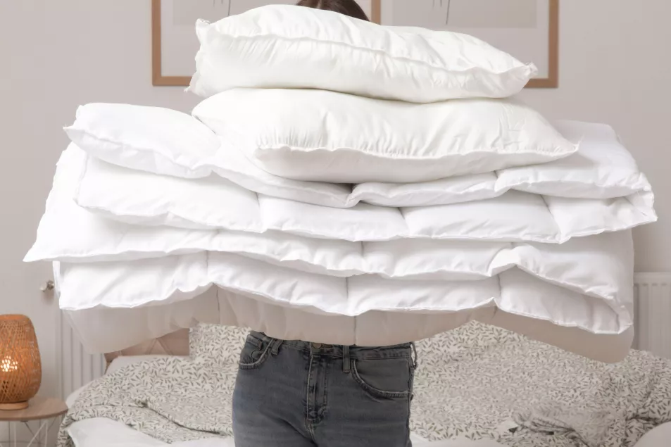 Woman holding pile of pillows and duvet 