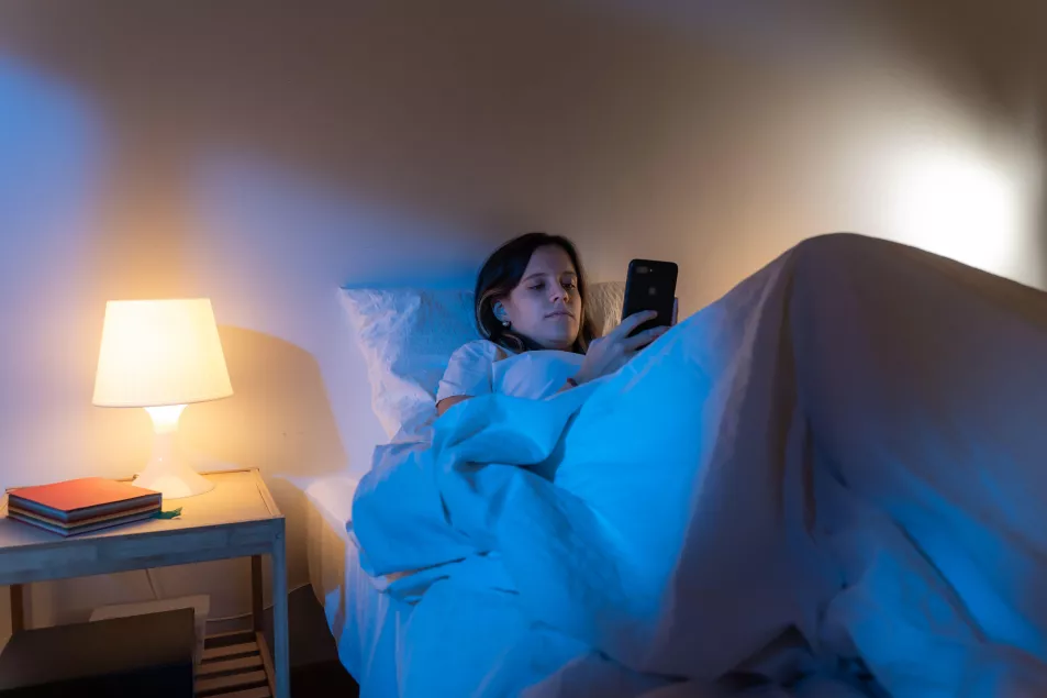 Girl looking her smart phone doom scrolling on bed in the middle of the night