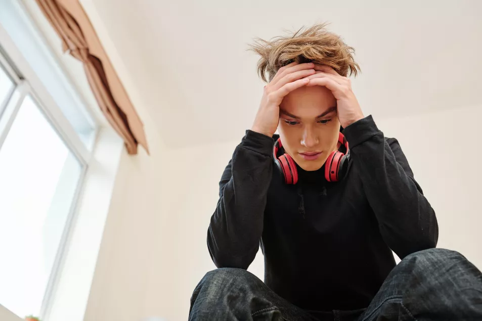 Teenage boy with headphone around his neck looking stressed