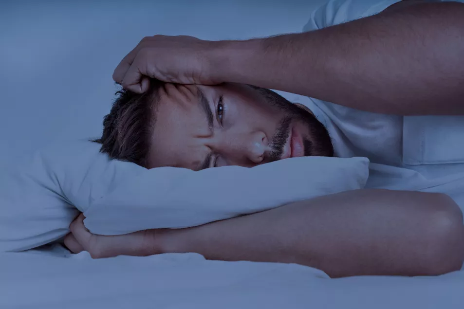 Young man lying in the bed suffering from insomnia