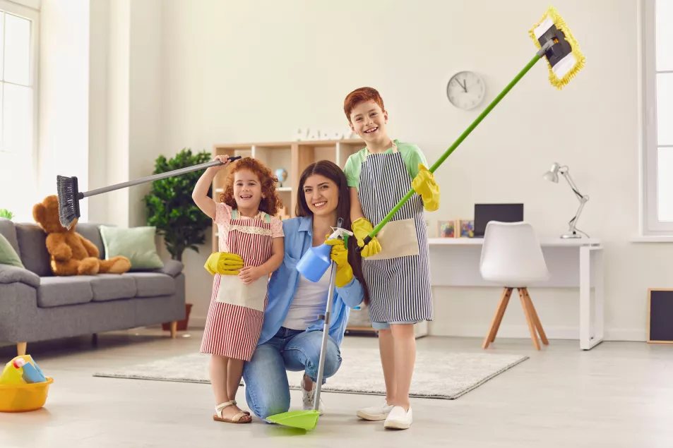 Happy mum and kids with floor mops and dustpan smiling and looking at camera after a big clear-out