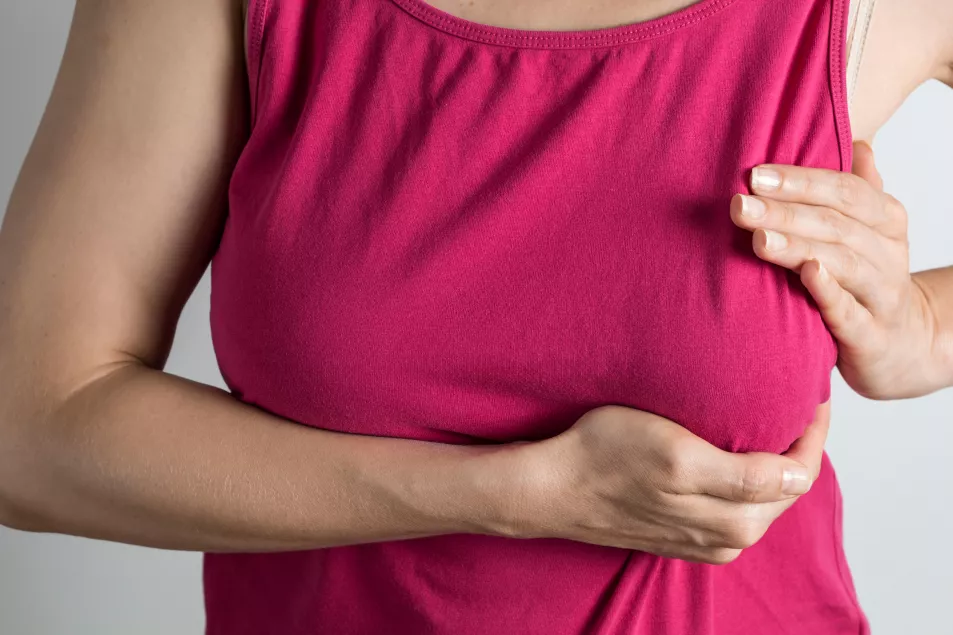 Woman wearing a pink Tshirt checking her breast for lump