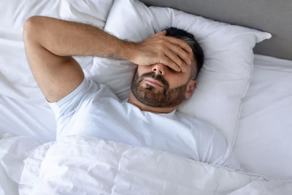 Man struggling to sleep in bed with his hand over his eyes 