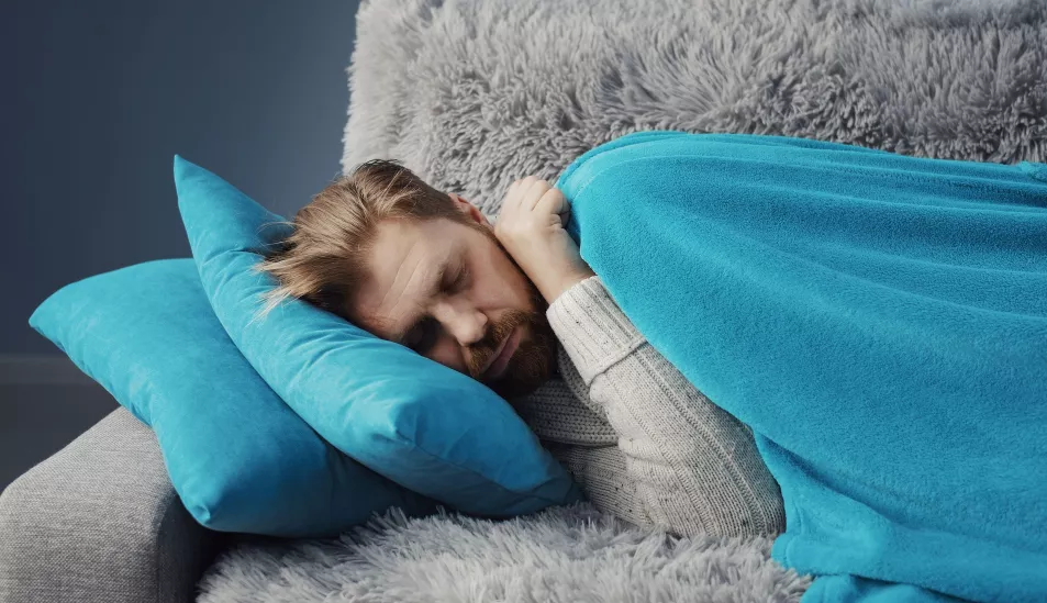 Ill man napping on a grey sofa wrapped in a blue blanket