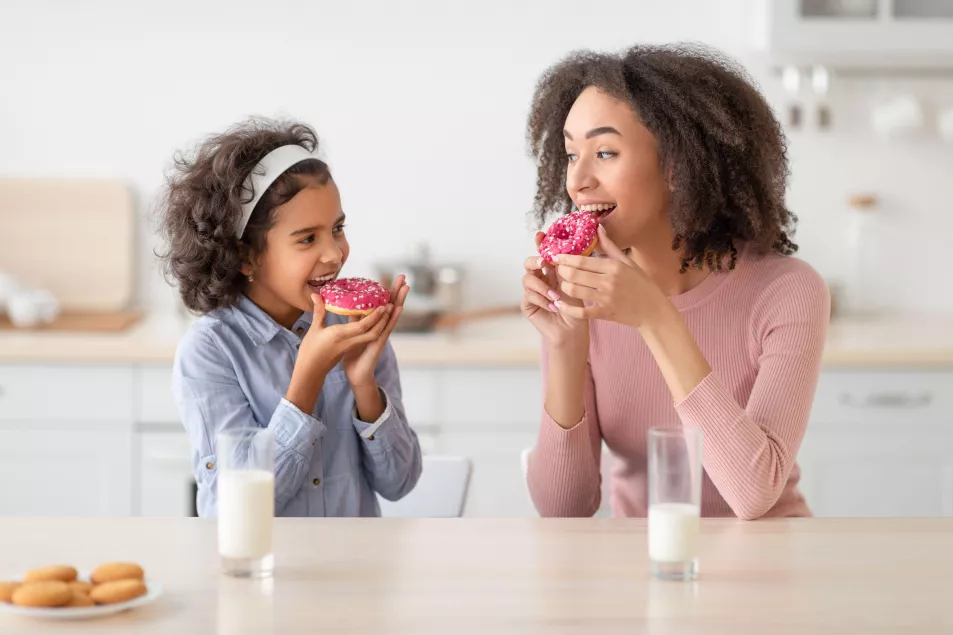 Mum and daughter eating doughnuts in the kitchen