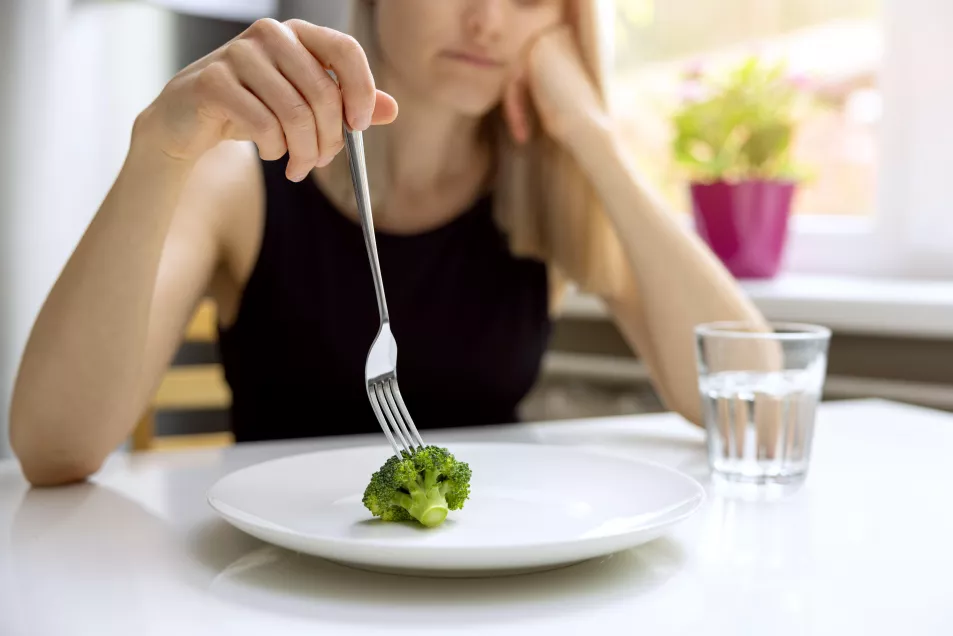 A young woman picking up a single piece of broccoli with her fork 