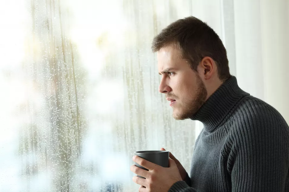 An unhappy man looking at the rain through a window