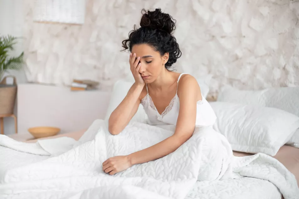 A tired woman sitting up in bed with her hand on her face