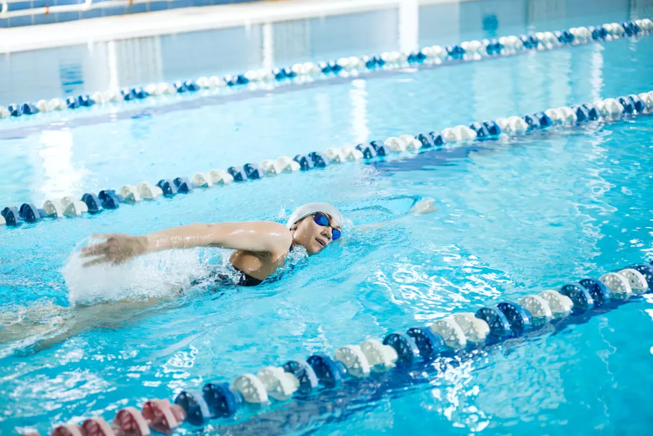 Young girl in goggles swimming front crawl in a swimming pool 