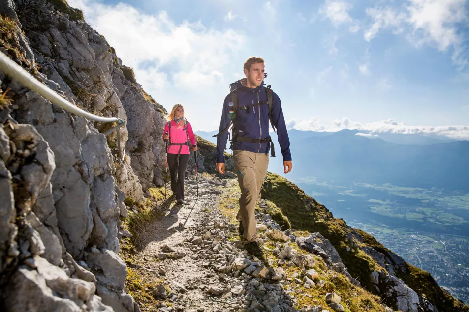 Young man and woman hiking on a mountain trail with a safety rope