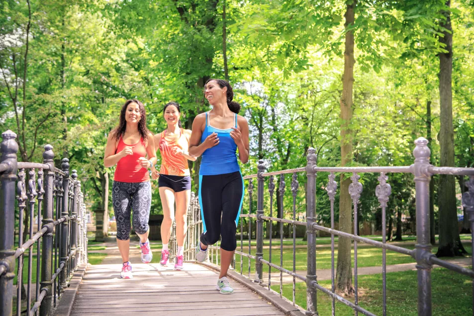 A group of three women jogging by a river in a park 