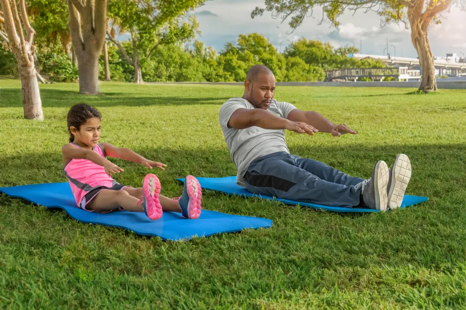 Father and daughter on yoga mats next to each other in a park doing sit ups