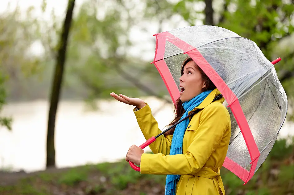 Young woman under an umbrella putting her hand out to feel the rain