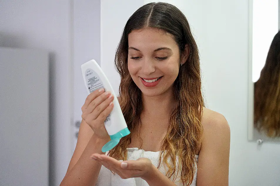 Young woman in towel squeezing some leave-in conditioner onto her hand 