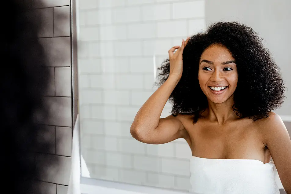 Young woman with curly dark hair looking in the mirror smiling 