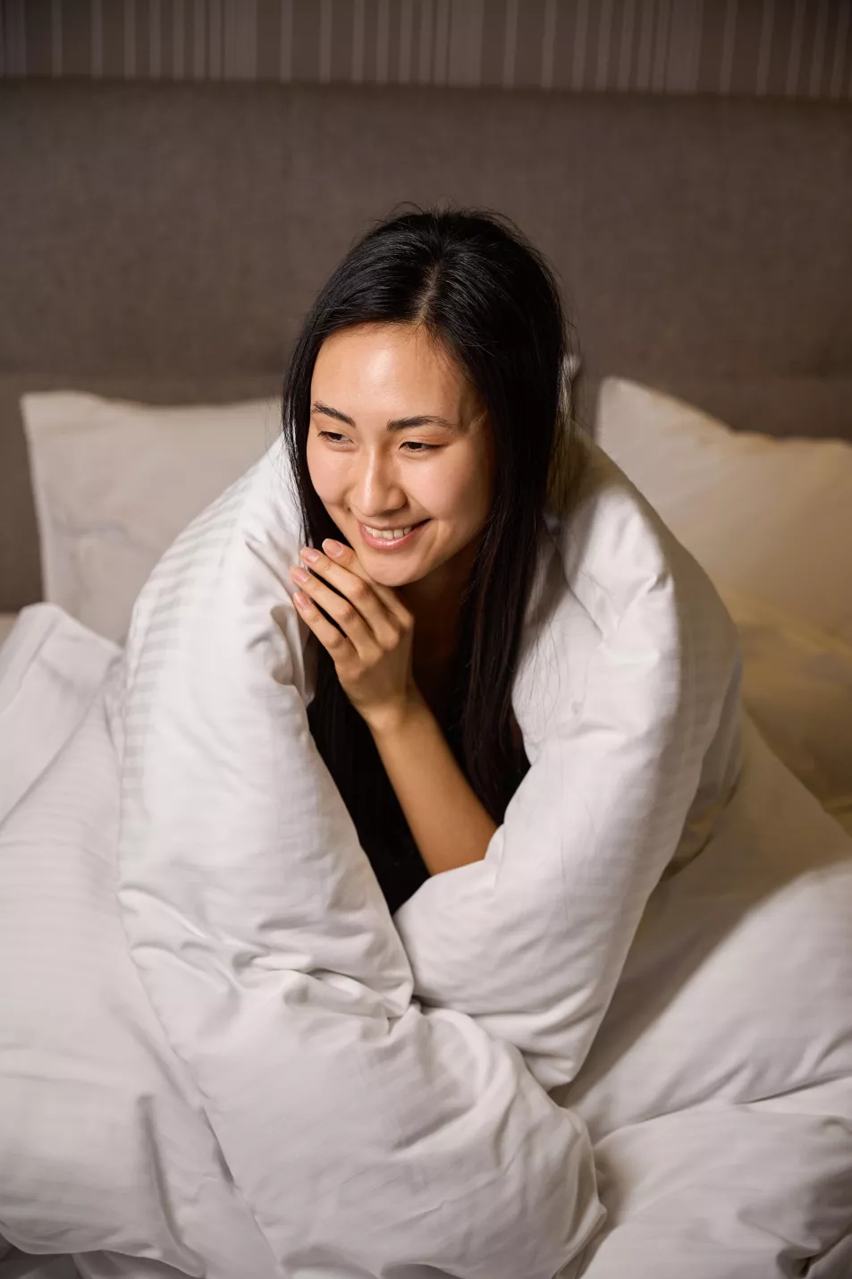 Young woman wrapped up in a white duvet smiling 