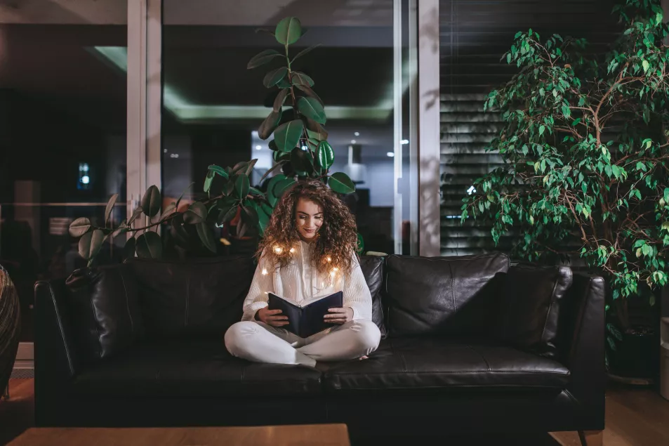 Young woman reading book on a sofa in the evening 