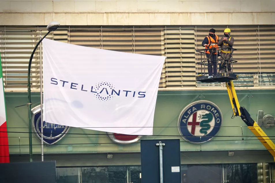 Workers next to a Stellantis flag and an Alfa Romeo sign 