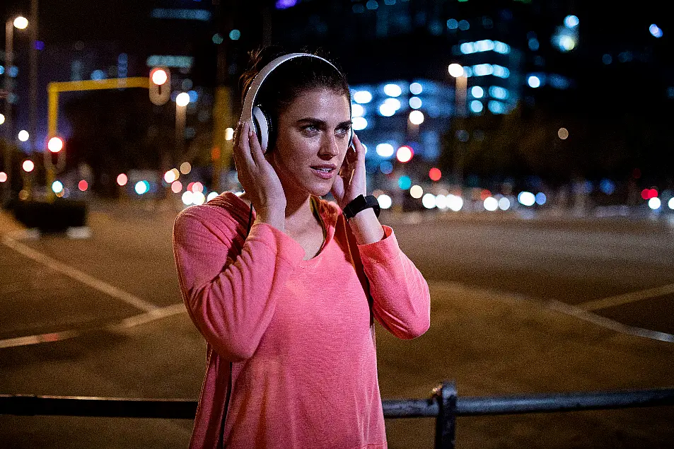 Woman wearing pink gym top putting headphones on before she starts running in the dark