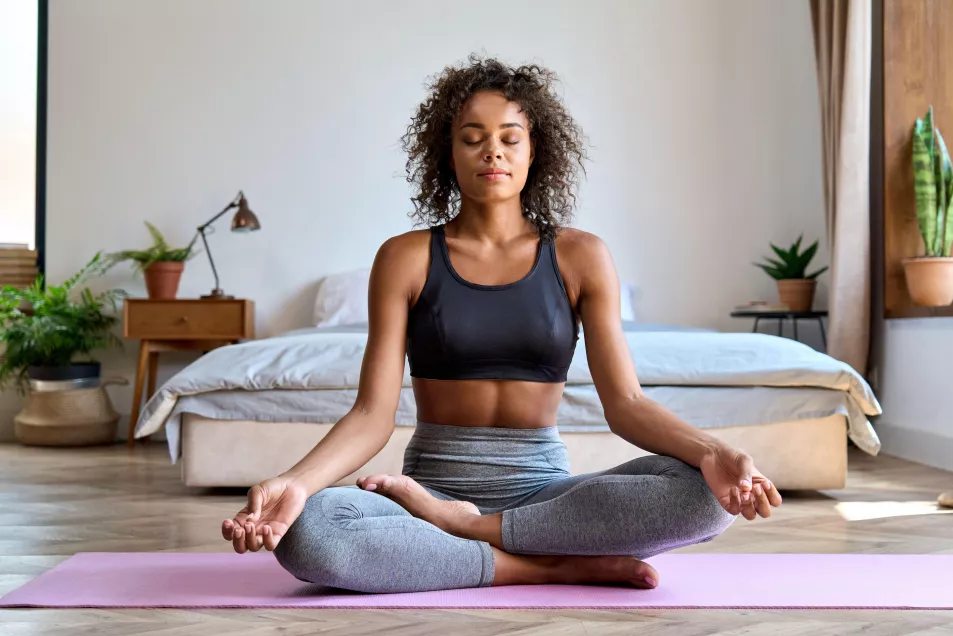  Young woman wearing sports kit mediating on a yoga mat at home 