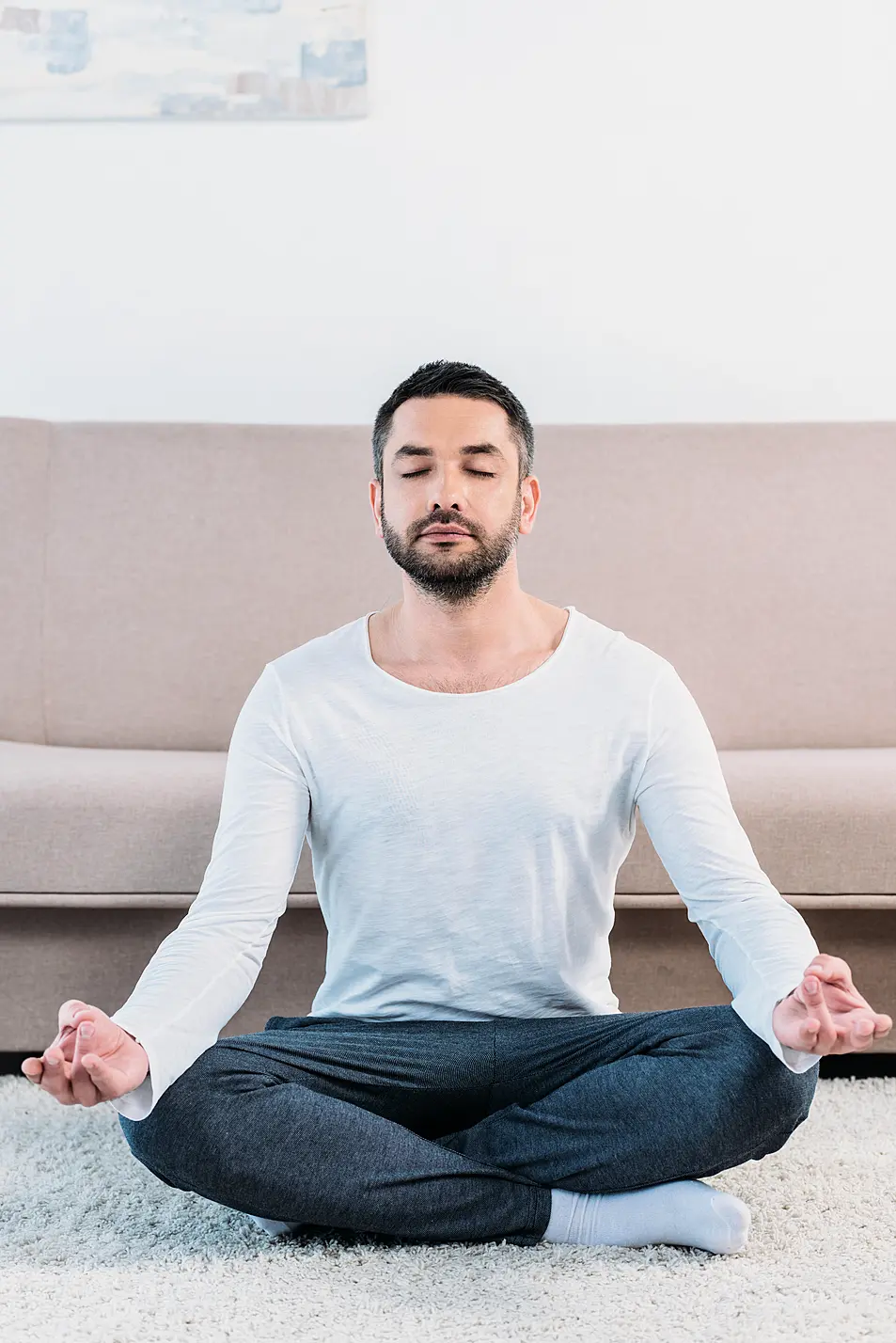 Man sat on the floor in a living room cross-legged meditating 