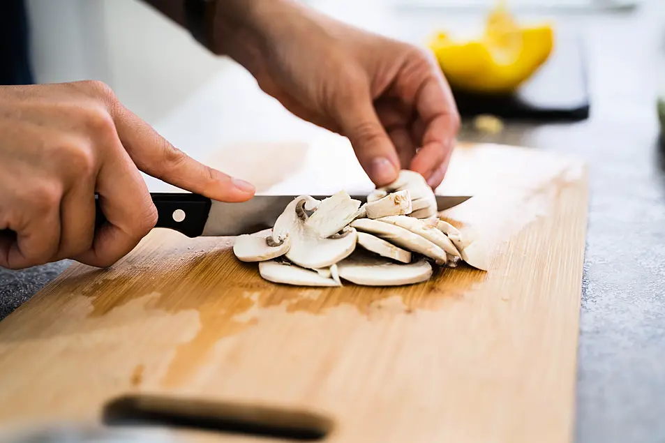 Woman cutting up mushrooms on a wooden chopping board