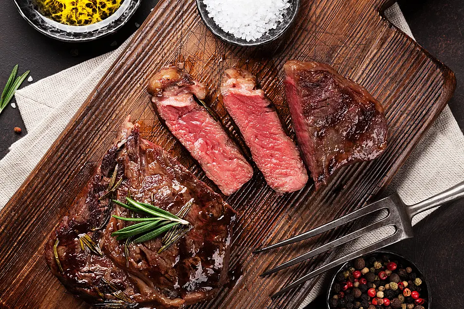 Grilled ribeye steak served on a wooden board next to herbs and spices 