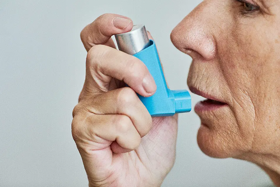 Close up photo of a woman about to take a puff from a blue inhaler