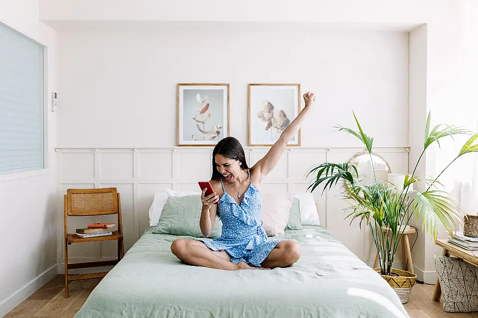 Happy young woman celebrating online success on mobile phone at home