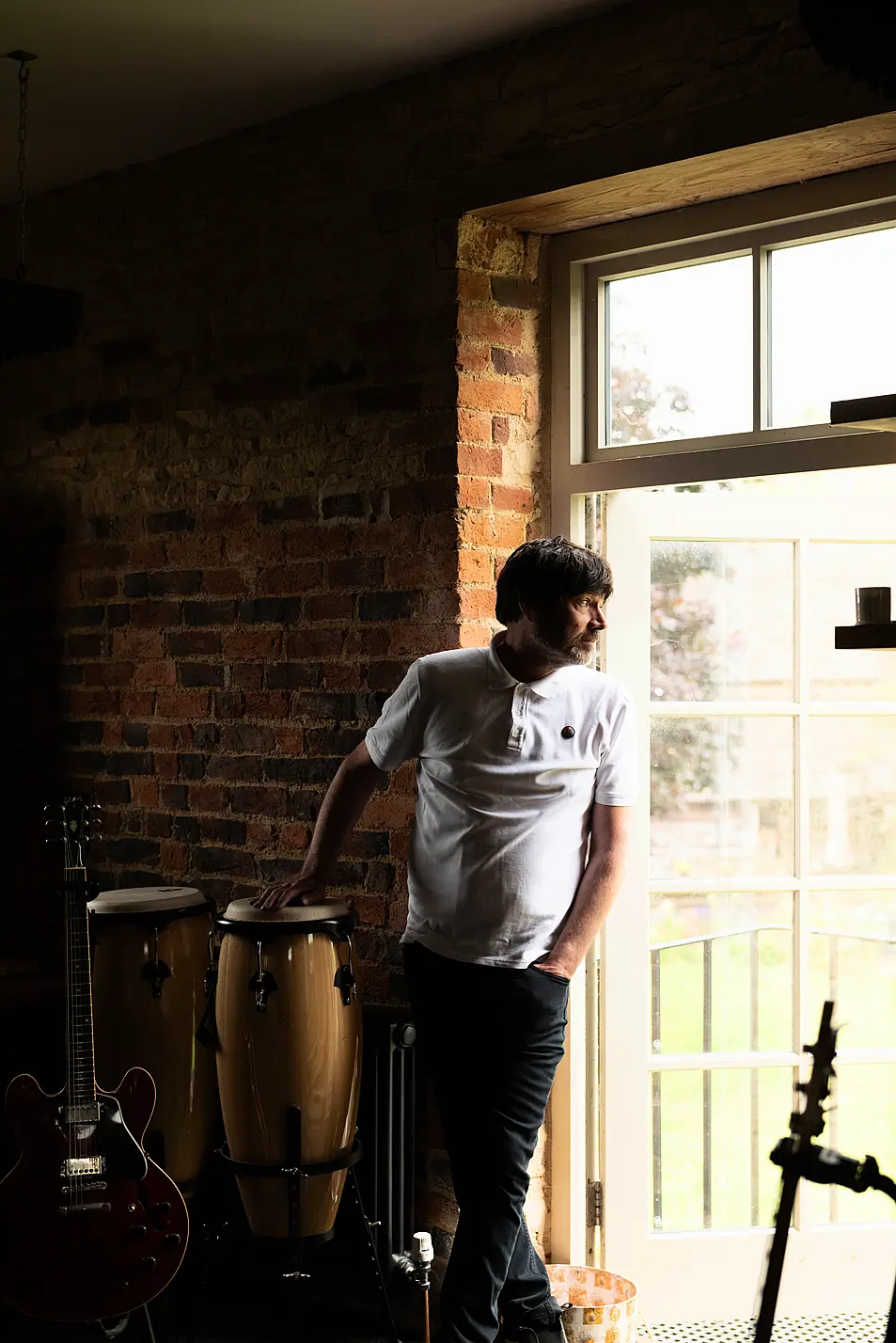 Alex James looking out a window wearing a white T-shirt.