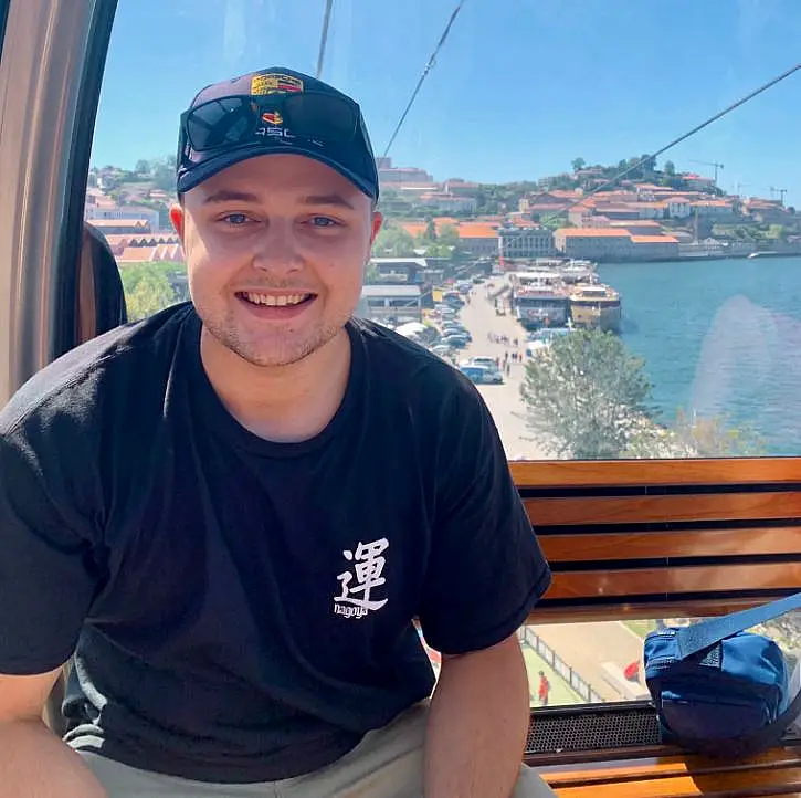 A young man wearing a baseball cap with a coastline behind him 