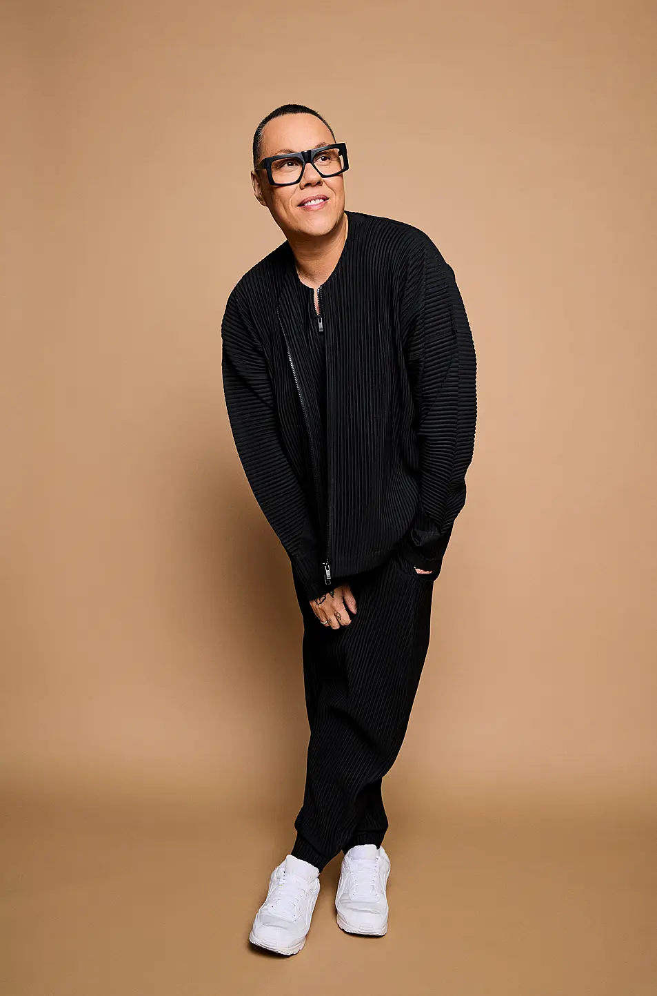 Gok Wan stands cross legged on shoot in black tracksuit