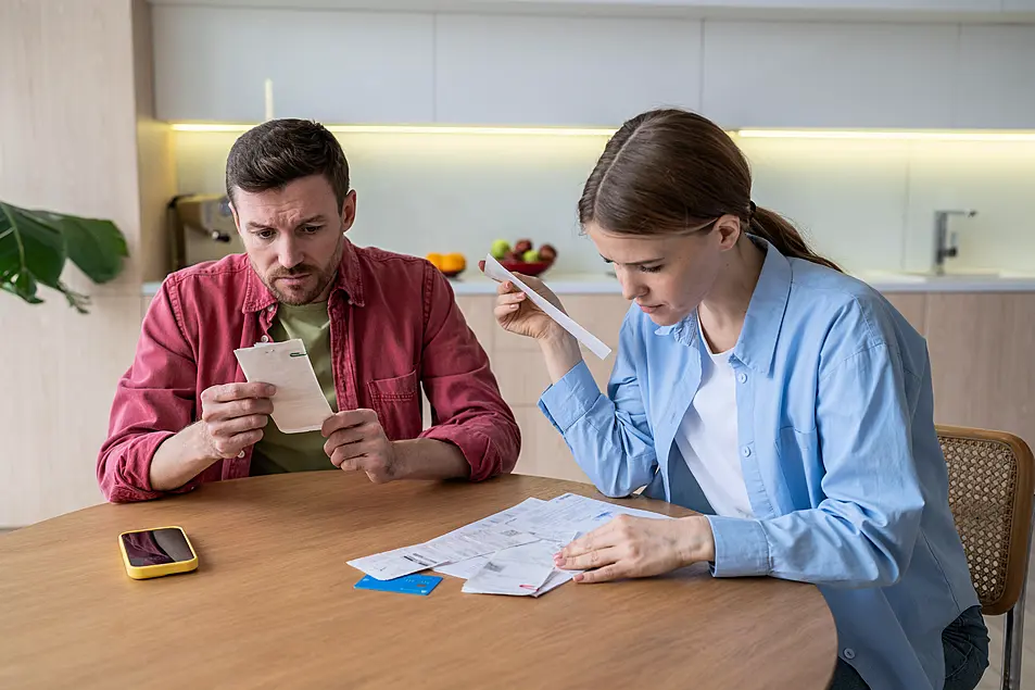 Couples sit at kitchen tables with bills stressed