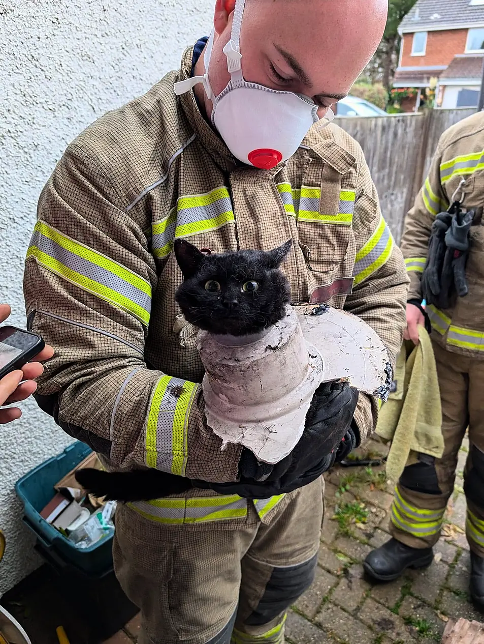 Firefighter folding a black cat with part of a drainpipe wrapped around its neck after it became stuck in the tube