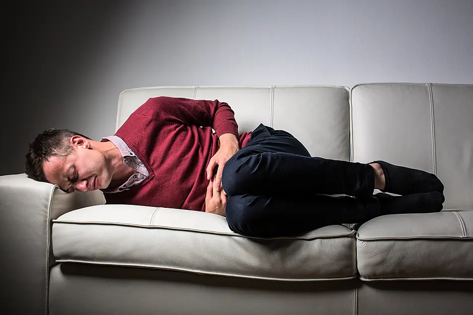 Man lying on a sofa experiencing stomach pains 